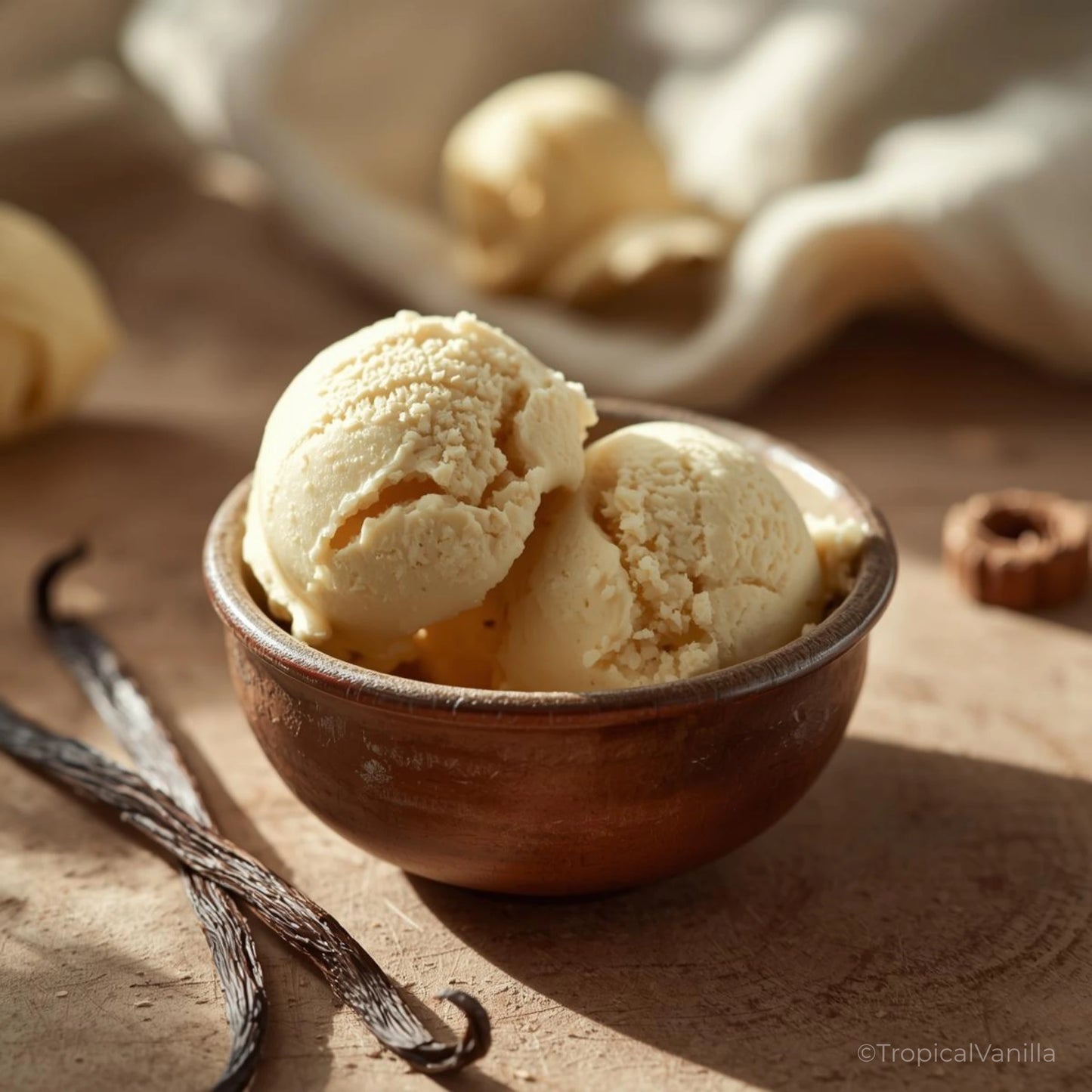 Two scoops of vanilla ice cream in a wooden bowl on a sandy surface with vanilla beans.